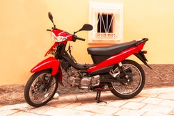Moped, red scooter stands parked against the wall of the house