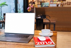 Blank screen laptop with mouse and coffee cup and notebook with Year 2019 calculator on table in cafe.