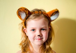a cute little girl with blonde hair, in the ears of a tiger gently smiles.