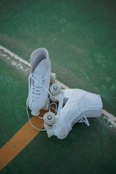 High angle shot of pair of white roller skates together with untied laces on a green court.