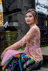 Young Balinese girl dressed in colorful batik sarong poses in front of a temple, Bali, Indonesia 