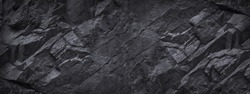Black stone background. Dark gray grunge wide banner. Black and white background. Mountain texture. Close-up. Volumetric. The rocky backdrop. Abstract black rock background. Copy space.