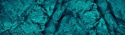Blue green rough rock texture. Toned. Cracked crumbled mountain surface. Close-up. Dark turquoise stone background with copy space for design. Wide banner. Panoramic.