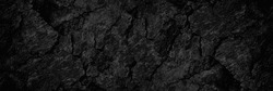 Black rock texture. Rough mountain surface with cracks. Close-up. Dark stone background with space for design. Grunge. Banner. Wide. Long. Panoramic. 