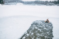 Winter swimming. Woman in frozen lake ice hole. Swimmers wellness in icy water. How to swim in cold water. Beautiful young female in zen meditation. Swimming clothes. Nature lake. Place for text