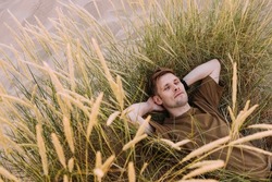 Young man laying in beach sand grass. People fatigue from sunburn and work. Summer sleeping and relaxation techniques. Vitamin D sunbathing. Man power nap with eye closed. Rest after work from home
