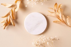 Dry natural grass, leaves and flowers frame with white marble podium, beauty and fashion concept mock up on beige background flat lay, top view, copy space