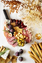Meat, cheese and snackes plate, board and grissini with dry flowers bouquet, on white background, flat lay, top view, vertical