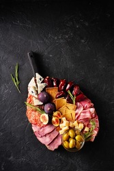 Meat, cheese and snackes plate, board and grissini on black background, flat lay, top view, vertical