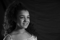 Side portrait of smiling teenage girl without looking at the camera with black background and curly hair. Black and white horizontal image. Concept of emotions.