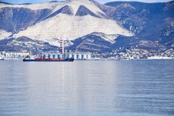 Against the backdrop of mountains, an oil tanker and barrels for oil products stand in the bay. Sea international, cargo port