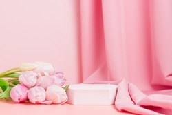 Podium with pink tulips and textile fabric drape at the background. Display for spring cosmetic or product presentation