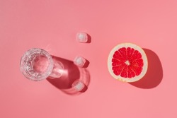 Glass of water, ice cubes and grapefruit with harsh shadows, summer refreshment, minimal concept, cocktail with ice flat lay
