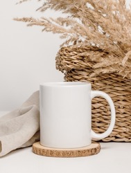 Mockup mug with dry grass and wicker container decoration at the background. Mug with copy space for text and design. Cozy, home decoration concept