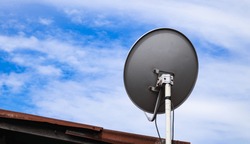 Satellite dish on roof to receive a TV signal with sky background