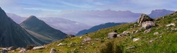 Panorama of the Alpine mountains. Ridges and peaks are visible in the background. Large and small stones lie on the grassy slope.
