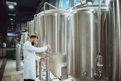 A handsome brewer examines beer from tanks in a brewery