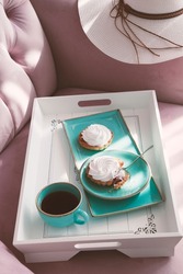 Beautiful breakfast tray setting from a cyan blue ceramic dishes on a white wooden breakfast tray on a pink sofa in a window lightning on a lazy afternoon