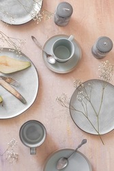 Empty grey uneven ceramic dish collection on a light pastel peach pink table with cutlery, candles and other decorative elements