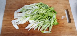 Cutting green onion into diagonal lines is on a tree chopping board.