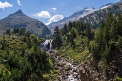 Forau d'Aigualluts waterfall with mountains and Aneto snowy peak in the background, in Benasque, Huesca, Spain. Alpine landscape in Posets Maladeta natural park, Spanish Pyrenees