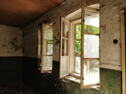 Inside abandoned house. View on broken windows without curtain. Grunge scene. Through the old wooden frames with broken glass breaks warm sunlight. The concept of change, abandonment, uselessness.