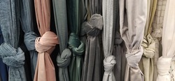 Curtain and fabric for drapery and interior decoration. Samples of fabrics in the store are hung vertically and tied in knots. White, gray, green, peach, champagne and yellow curtains in the showcase