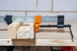 A woodworking sash clamp used to temporary hold wood tightly together whilst gluing up with wood glue . Close up view with wooden  bench background.