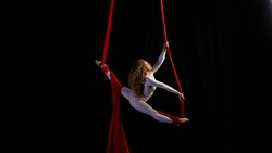 Professional aerialist circus performer on red bright aerial silks performs balance on a splits