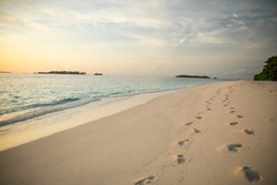 Serene tropical beach at sunset with 2 sets of footprints i n sand
