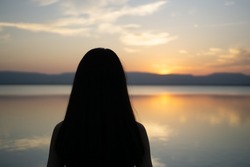 silhouette of girl looking at sunset time as background with lake and mountain,selective forcus on girl
