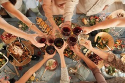 High angle view of group of people holding glasses and toasting with red wine at the table during dinner