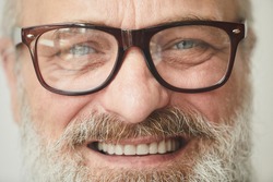 Close-up of senior bearded man in eyeglasses smiling at camera