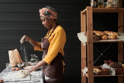 African baker in apron making a dough and baking homemade bread while working in the bakery