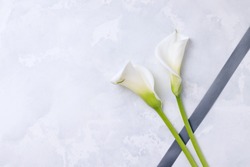 White flowers callas with mourning ribbon on a concrete background. Copy space. The concept of mourning and sorrow