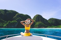 Rear view of adult traveling woman sit and relax on the sailing boat wear yellow bikini blue sky and sea. Summer vacation island domestic trip at Maya bay. Krabi, Thailand