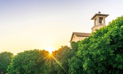picturesque view from evening garden to a beautiful sunset withstreaming sunbeams through trees and nice building on the foreground and sun with clear sky on background
