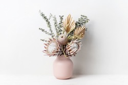 Beautiful dried flower arrangement in a stylish pink vase. In the flower bunch is pink King Proteas, Banksia, Eucalyptus leaves and golden Palm frond photographed on a white background.