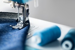 Sewing machine with denim and thread for sewing, close-up. The working process. Part of a sewing machine with blue cloth.