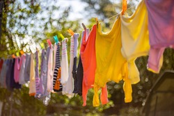 Baby cute clothes hanging on the clothesline outdoor. Child laundry hanging on line in garden on green background.Baby accessories.
