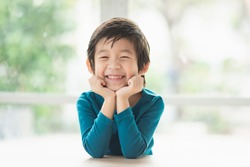 Cute Asian child resting chins on hands on wood table 