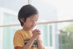 Cute Asian child boy praying with eyes closed in the morning at home