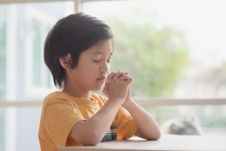 Cute Asian child boy praying with eyes closed in the morning at home