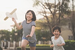 Cute Asian children playing cardboard airplane together in the park outdoors