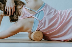 Upper body details of woman rolling lower armpit on a cork massage roller to release tension in side body muscles. Concept: self care practices at home, sustainable props, myofascial release