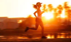silhouette with motion blur of a woman athlete running at sunset or sunrise. fitness training of marathon runner.