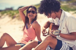 Cute hispanic couple playing guitar serenading on beach in love and embrace