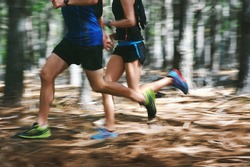 Couple running fast through the forest on trail run with motion blur