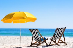 Pair of sun loungers and a beach umbrella on a deserted beach; perfect vacation concept 