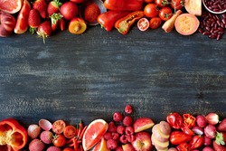 Food frame constructed with red fruits and vegetables, fresh raw organic produce on dark distressed background
